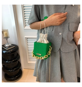 Detail of vibrant green woven bucket bag with golden chain strap and drawstring liner