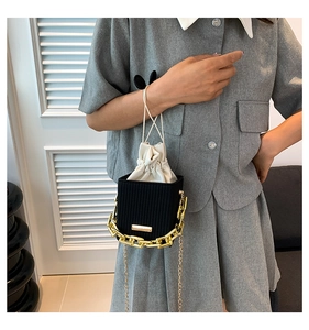 Detail of black structured crossbody bag with gold chain and drawstring inner pouch
