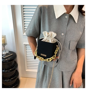 Detail of a black woven square bag featuring a gold chain handle and white drawstring liner