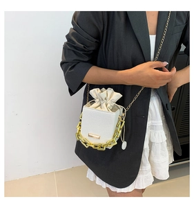 White bucket bag featuring a gold chain and drawstring inner pouch on a shoulder strap