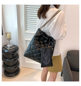 Detail of black quilted leather tote bag featuring chain strap and small matching pouch