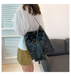 Model wearing a black quilted tote bag with golden chain strap and matching pouch