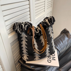 Black and white woven bucket bag with fringe trim and brown leather handles for women