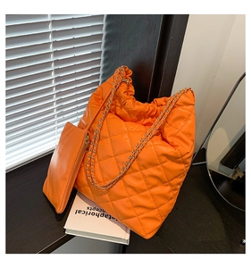 Macro detail of orange quilted leather tote bag with gold chain strap and mini pouch
