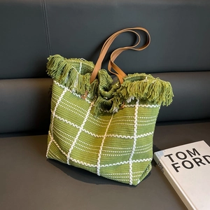 Green woven tote bag with fringe and brown leather handles in bohemian resort style