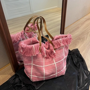 Pink woven tote bag with white checkered pattern, pink tassels and brown leather handles