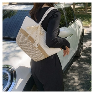 Close-up of woven tote bag featuring cream lace bow detail and textured straw finish