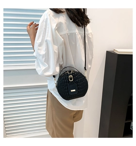 Detail of black round crossbody bag with crocodile texture and gold hardware on a model