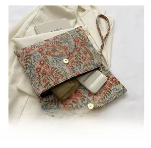Floral jacquard envelope clutch bag showing storage capacity with a matching wrist strap