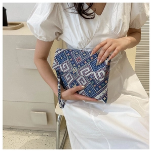 Detail of woven clutch with geometric patterns, wrist strap and gold clover buckle