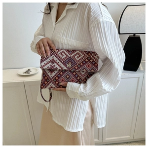 Detail view of ethnic geometric woven clutch with red embroidery and golden buckle