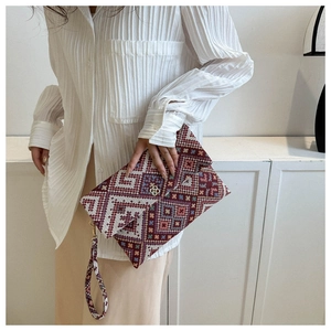 Ethnic embroidered clutch bag with geometric patterns and golden clover clasp on model