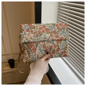 Close-up of floral tapestry envelope clutch with golden clover buckle and wrist strap