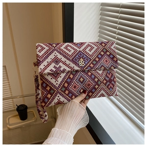 Detail of colorful ethnic geometric woven envelope bag with gold floral hardware and strap