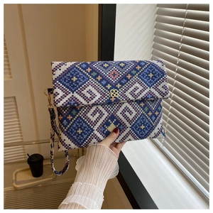 Detail of woven clutch bag featuring colorful geometric patterns and gold clover clasp
