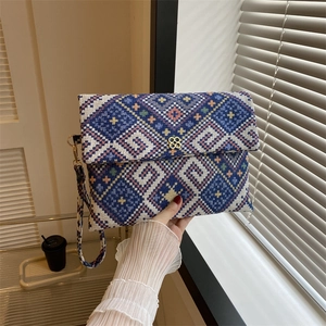 Handheld woven clutch bag with blue geometric patterns and gold clover buckle for women