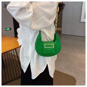Détail d'un sac demi-lune vert avec chaîne dorée épaisse porté par un mannequin