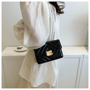 Détail du sac noir matelassé en V avec chaîne dorée porté par un mannequin