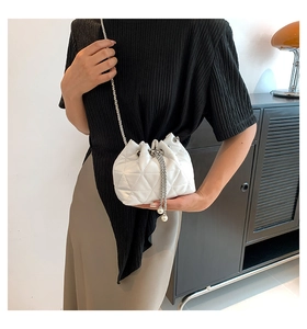 Detailed view of white quilted bucket bag featuring a silver chain strap and pearl tassels