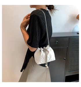Detail of white quilted bucket bag featuring a drawstring closure and pearl accents