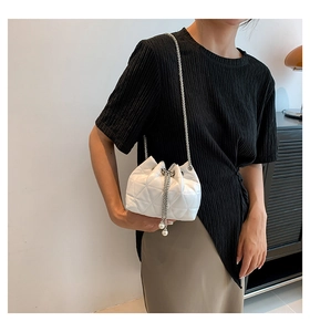 Detail of white quilted bucket bag featuring silver chain straps and large pearl tassels