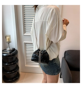 Detail of black quilted bucket bag featuring silver chain strap and pearl drawstring