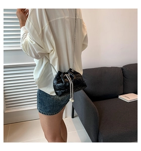 Detail of black quilted bucket bag with silver chain and white pearl drawstring accents