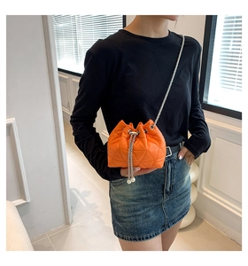 Detail of bright orange quilted bucket bag with pearl drawstring and silver chain strap