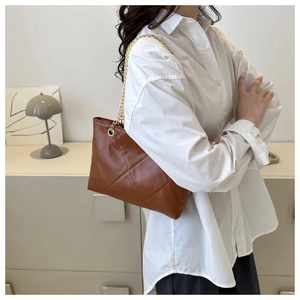 Sac bandoulière marron en cuir matelassé avec chaîne dorée sur une chemise blanche