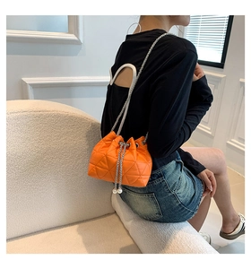 Detail of orange quilted bucket bag with chain strap and pearl drawstring charms