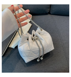 Detail view of white quilted bucket bag with silver chain and elegant pearl drawstrings