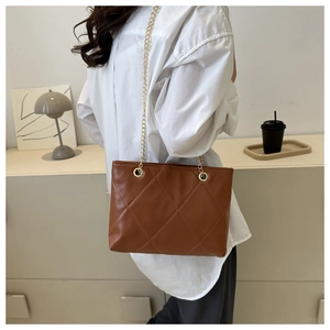 Détail du sac bandoulière matelassé marron avec chaîne dorée porté par un mannequin