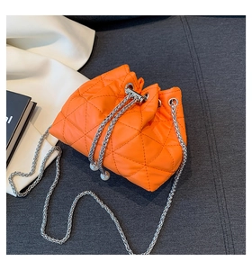 Detail of bright orange drawstring bucket bag with quilted texture and pearl charm