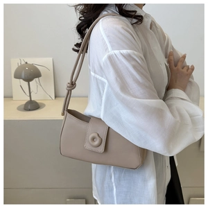 Minimalist beige baguette bag showing knot detail strap and magnetic clasp on a shoulder