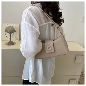 Detail of the minimalist beige leather bag with a round buckle and knotted shoulder strap