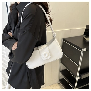 White minimalist underarm bag with decorative round buckle worn by a model in a modern office