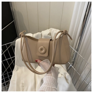 Detail of the knotted shoulder strap and round flap buckle on a beige leather underarm bag