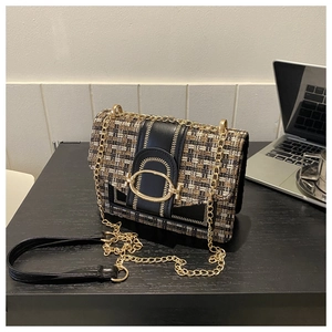 Detail of tweed and black leather crossbody bag with a vintage gold buckle on a desk