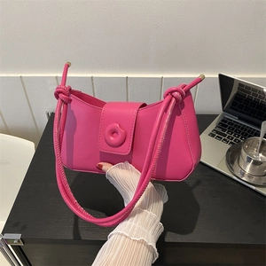 Pink glossy leather baguette shoulder bag with knotted strap on a desk workspace