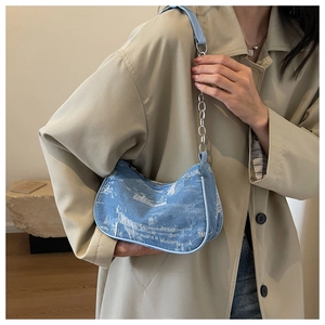 Close-up of light blue denim baguette bag with distressed texture and silver chain strap