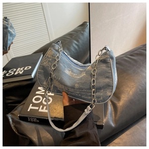 Detail of blue denim shoulder bag with silver chain and frayed edges on leather sofa