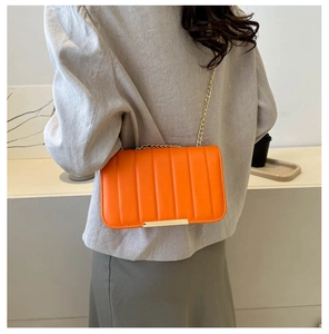 Detail of orange quilted crossbody bag with gold chain strap on female model