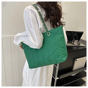 Green quilted tote bag with chain strap shown on model in an office setting