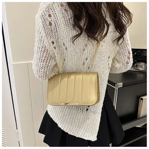 Detail of a shiny gold quilted chain bag with vertical stitching and metal hardware