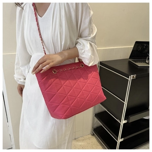 Detail of fuchsia quilted shoulder bag with gold chain strap shown on a model