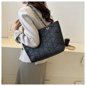 Detailed side view of a black quilted tote bag with silver metal chain straps on a model