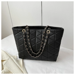 Detail view of black tote bag featuring triangular quilted stitching and golden chain strap