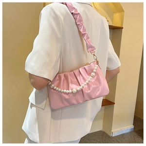 Détail du sac à bandoulière rose plissé avec chaîne de perles porté par le mannequin