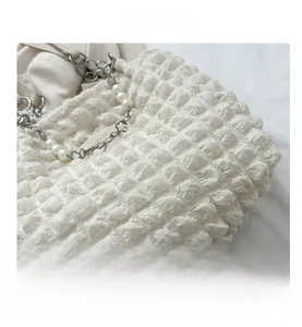 Detail of white popcorn texture fabric with silver chain and pearl strap of a tote bag