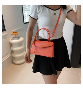Orange croc-embossed small crossbody bag shown on model with neutral outfit